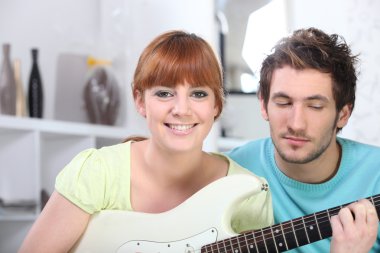 Red-haired girl playing guitar in bedroom with boyfriend clipart