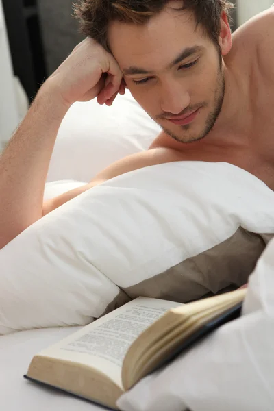 Jonge man ontbloot bovenlijf lezing in bed — Stockfoto