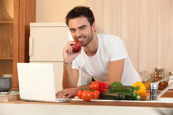 Homme dans la cuisine avec ordinateur portable et légumes — Photo