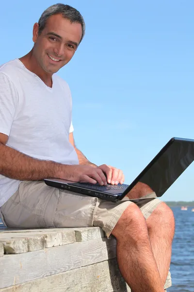 Uomo seduto su un molo utilizzando il computer portatile — Foto Stock