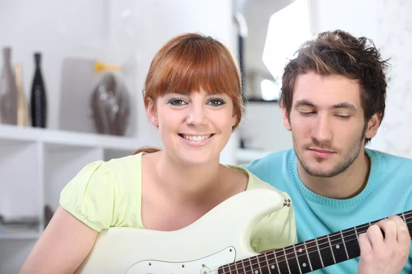 Ragazza dai capelli rossi che suona la chitarra in camera da letto con il fidanzato — Foto Stock