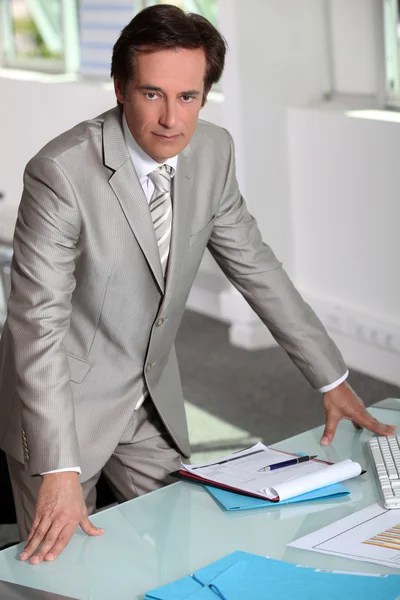 Człowiek w srebrno szary garnitur, celowo stoi przy swoim biurku — Zdjęcie stockowe