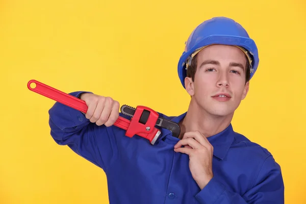 Portrait of young plumber holding adjustable spanner against yellow backgro — Stock Photo, Image