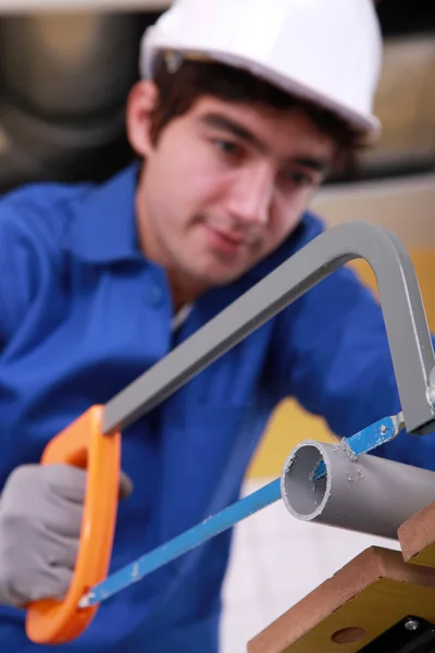 Joven está cortando un tubo de pvc con una sierra —  Fotos de Stock