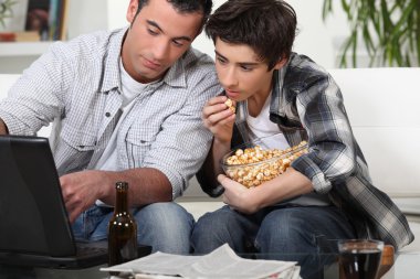 Young men looking with interest at a laptop clipart