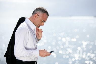 Businessman sending a text message by the seaside clipart