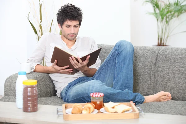 Mann liest und frühstückt auf dem Sofa — Stockfoto