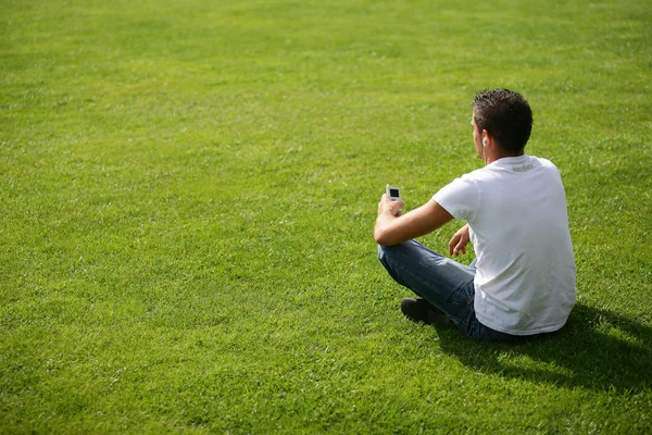 Mladý muž se uvolnil, sedět na trávě — Stock fotografie
