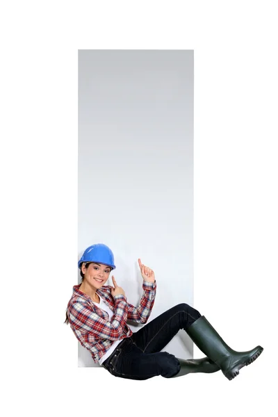 Construtor feminino sentou-se por cartaz em branco — Fotografia de Stock