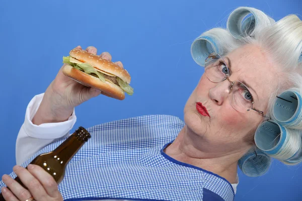一位老太太享受一个汉堡和一杯啤酒. — 图库照片