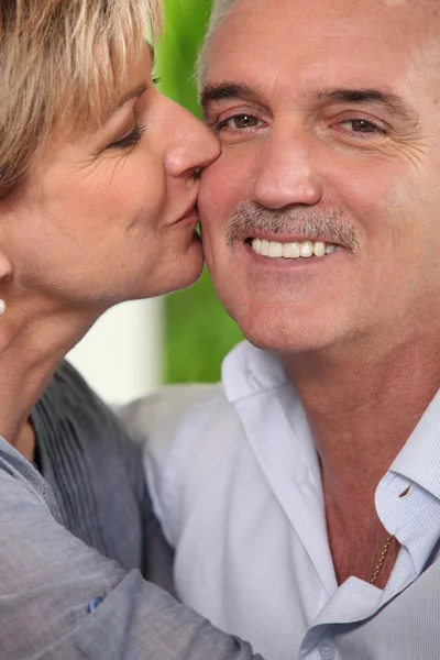 Volwassen vrouw een lachende man kussen op de Wang — Stockfoto