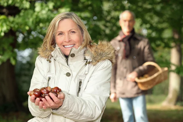 Reife Frau im Wald mit Mann zeigt Kastanien — Stockfoto