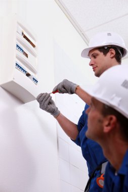 Two electrical workers installing fuse box clipart