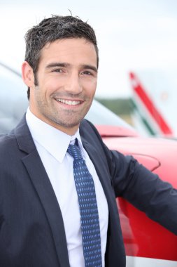 Smiling businessman standing next to a light aircraft clipart