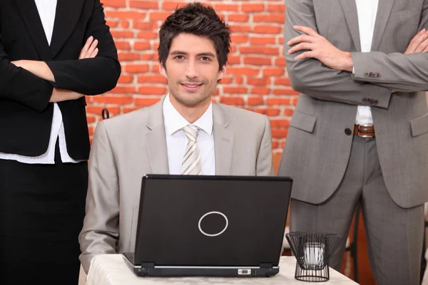 Man using a laptop flanked by in suits — Stock Photo, Image