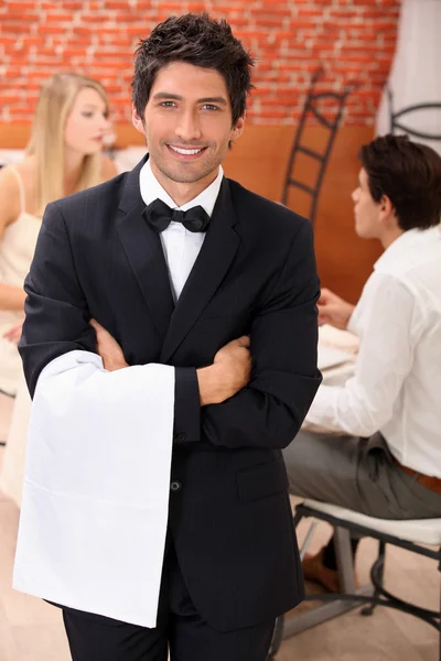 Καλά ντυμένος σερβιτόρος μπροστά στην κάμερα, πίσω από ένα ζευγάρι δείπνο στο παιχ — Φωτογραφία Αρχείου