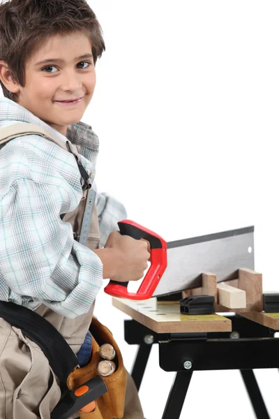 Genç çocuk bir yetişkin marangoz kesim ahşap testere ile giyinmiş. — Stok fotoğraf