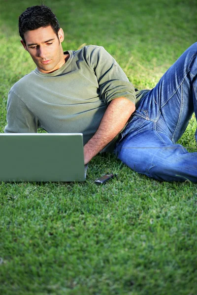 Man som ligger på gräset framför laptop — Stockfoto