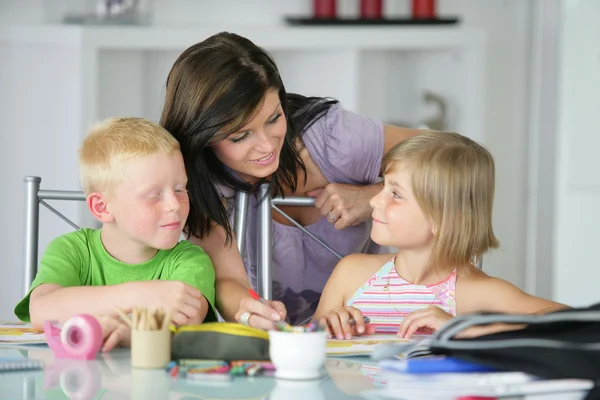 Mother watching brother and sister doing their homework — Stock Photo, Image