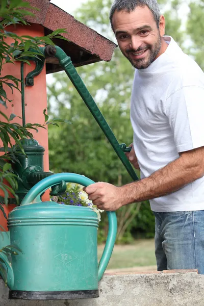 A mid aged man filling a watering can with a cast iron water pump — Stock Photo, Image
