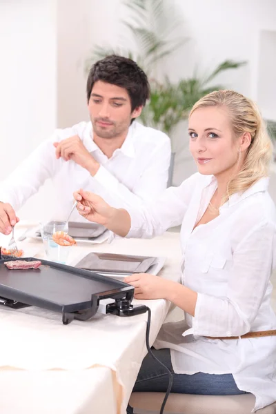 Couple cooking meat on a tabletop electric plate — Stock Photo, Image