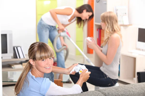 A woman vacuuming and two women playing video games — Stock Photo, Image