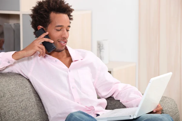 Young man sitting on sofa with laptop making a call — Stock Photo, Image