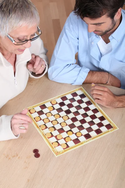 Äldre kvinna spela checkers med en ung man — Stockfoto