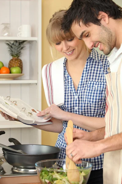 Woman and man smiling cooking using cookbook — Stock Photo, Image