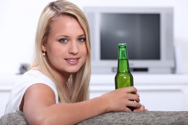 Mujer joven en casa con una botella de cerveza sin abrir —  Fotos de Stock