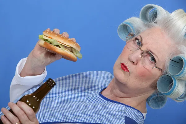 Yaşlı bir kadını bir hamburger ve bira keyfi. — Stok fotoğraf