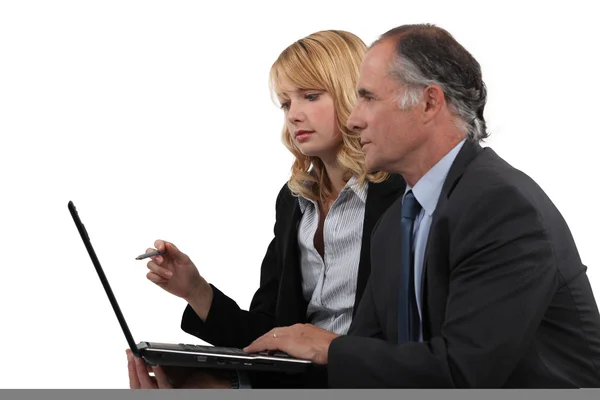 Senior executive working on laptop with junior female assistant by his side Stock Image