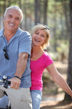 Man and woman riding a bike in the forest clipart