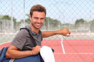 Man with sports bag stood by clay tennis court clipart