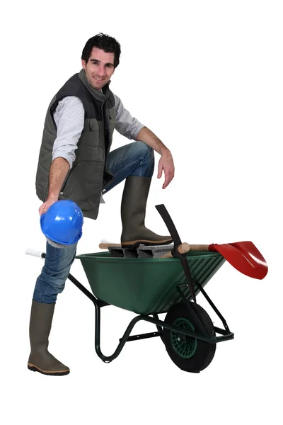 Construction worker showing off his hard hat, wheelbarrow and tools — Stock Photo, Image