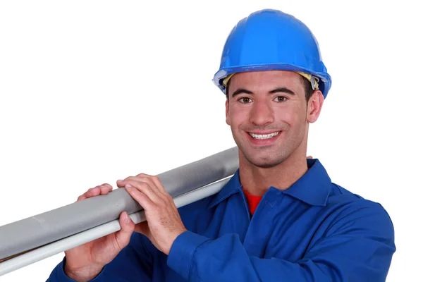 En byggnadsarbetare som bär en lång tub. — Stockfoto