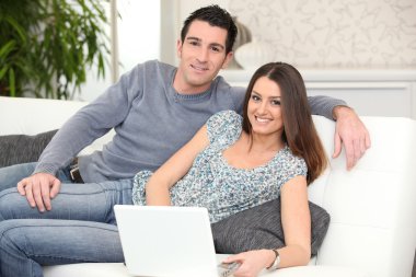 Duo lying on sofa with laptop clipart