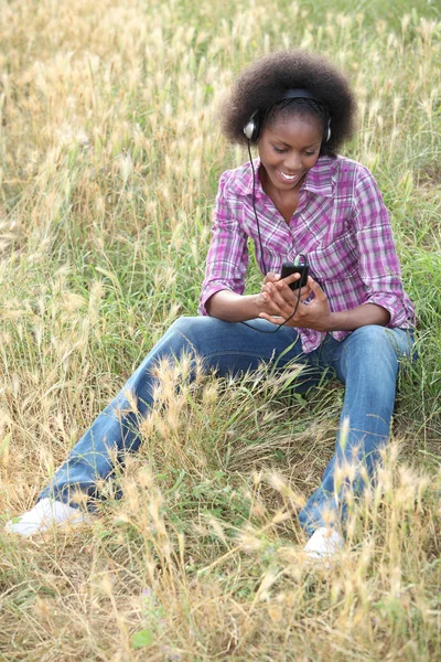 Femme noire assise dans l'herbe haute écoutant des chansons préférées — Photo