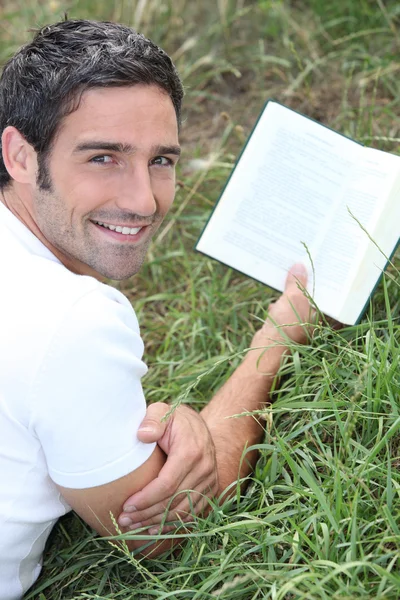 Uomo sdraiato sull'erba che legge un libro — Foto Stock