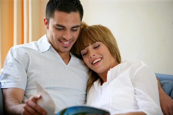 Happy couple reading a magazine on a sofa — Stockfoto