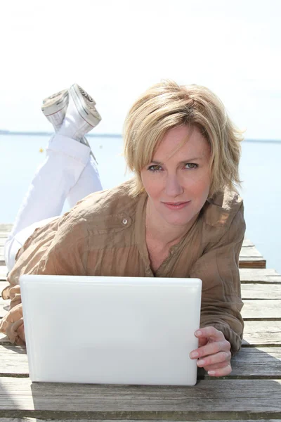 Woman lying on a jetty using a laptop computer — Stock Photo, Image