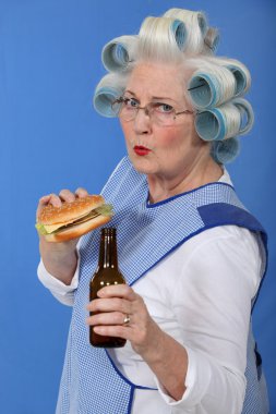 Funny picture of grandma with hair curlers relishing cheeseburger with beer clipart