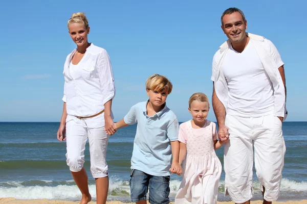 Jovem família caminhando ao longo de uma praia de areia — Fotografia de Stock