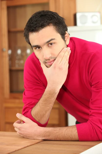 Молодой темноволосый парень на кухне в малиновом красном свитере — стоковое фото