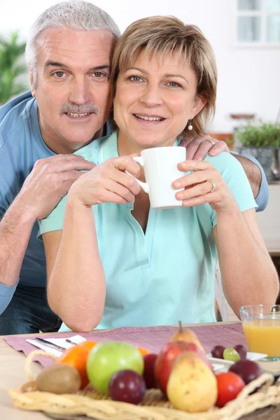 Зрелая пара улыбается за завтраком — стоковое фото