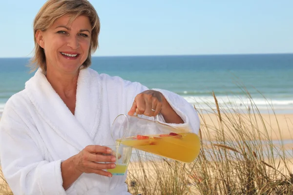 Vrouw schenkt zichzelf een glas sinaasappelsap in op het strand — Stockfoto