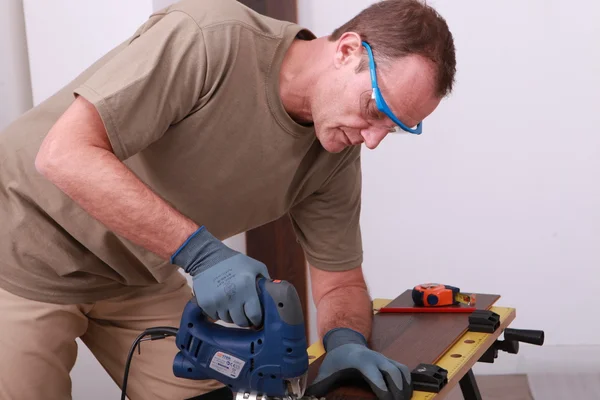 Uomo che usa una sega elettrica per tagliare una tavola da pavimento in legno — Foto Stock