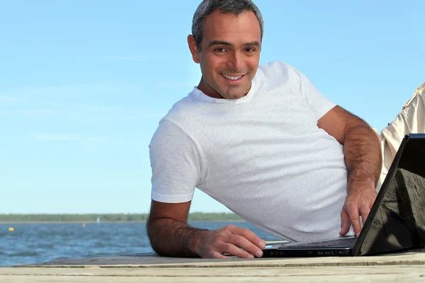 Homem olhando seu laptop junto ao lago — Fotografia de Stock