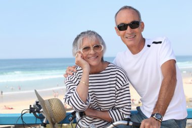 Senior couple riding bikes by the beach clipart