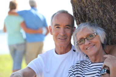 Relaxed older couple sitting in the shade of a tree on a summer's day clipart